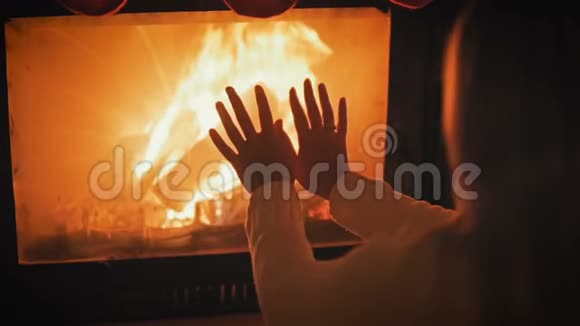夜间在燃烧的壁炉旁穿白色羊毛衫的年轻女子慢镜头升温视频的预览图