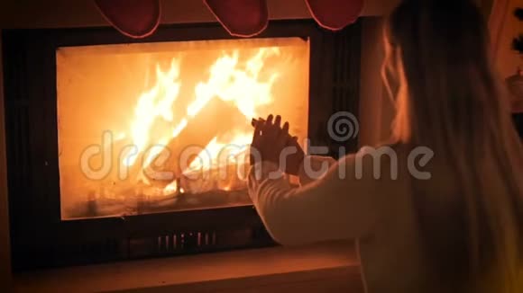 慢镜头的年轻女子坐在燃烧的壁炉旁暖和她的手视频的预览图