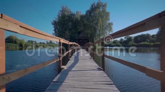 在一个阳光明媚的日子里一座长长的木桥通向河对岸的一间木屋视频的预览图