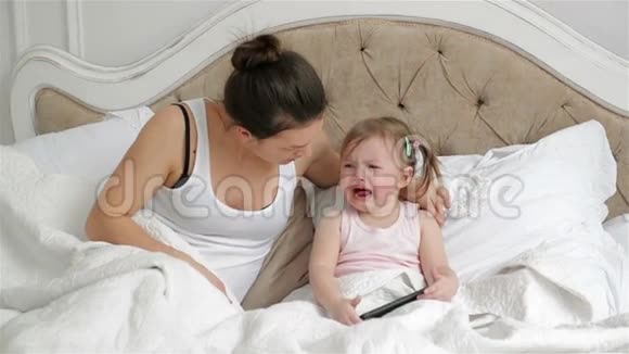 可爱的小女孩有两个马尾辫正在床上哭泣母亲正试图让女儿在卧室里平静下来视频的预览图