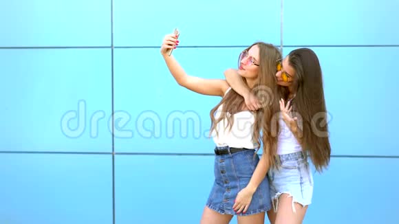 两位戴着太阳镜手持智能手机对着自拍的漂亮时髦女郎的时尚画像视频的预览图
