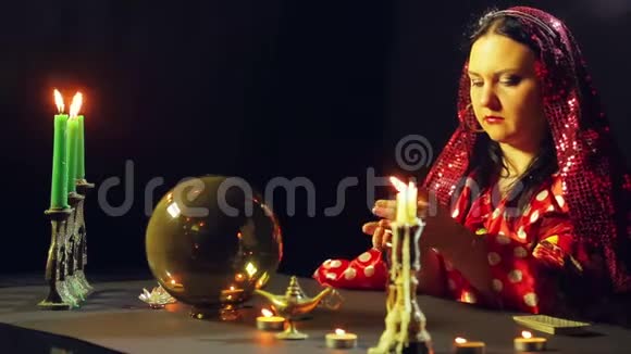 一个年轻的吉普赛人穿着红色的裙子在烛光下的桌子上读着石头上的未来平均计划视频的预览图