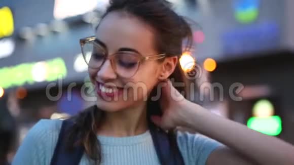 户外城市肖像一位戴眼镜的年轻成年美女在夜间城市灯光下在街上摆姿势视频的预览图