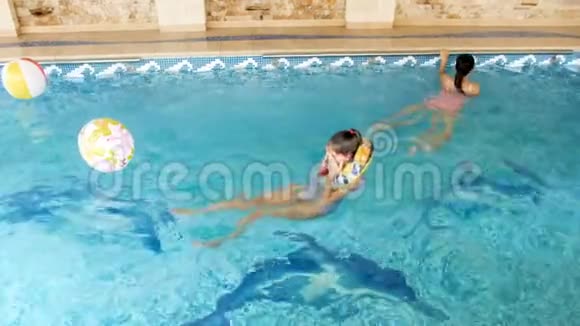 两个十几岁的女孩在室内游泳池里用充气彩色戒指游泳的4k视频视频的预览图