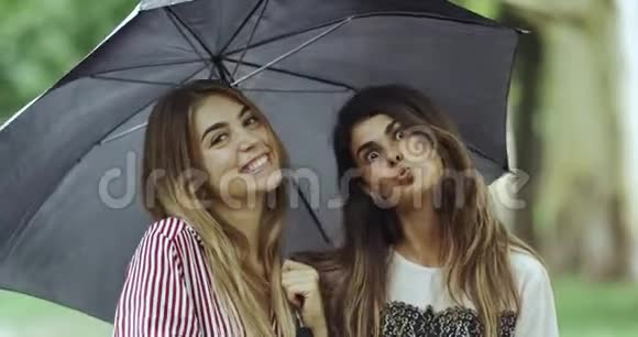 雨天的女士们在雨伞下直视镜头做着滑稽的脸视频的预览图