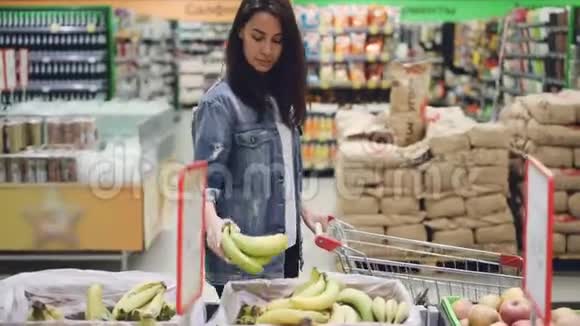 可爱的女孩快乐的顾客在超市里挑选水果买香蕉苹果和橘子然后把它们放进超市视频的预览图
