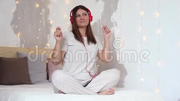 一个漂亮的女孩用红色的耳机听音乐用手机跳舞高清高清视频的预览图