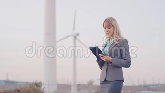 在windmills背景下穿着商务套装的商务女性在数字平板电脑中创建一个对象一个女人视频的预览图