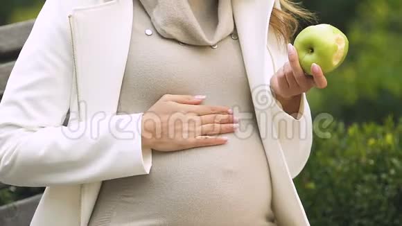 孕妇吃新鲜的绿苹果温柔地抚摸着肚子等待着宝宝视频的预览图