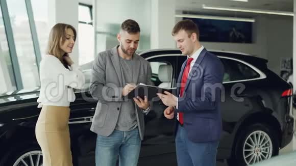 英俊的年轻人正在汽车经销商签订买卖协议从销售员那里拿到关键的fob然后给它视频的预览图