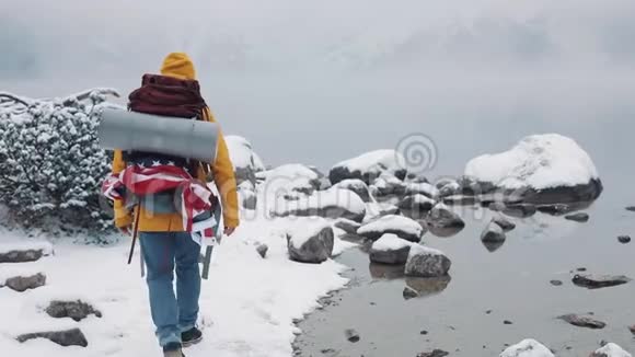 美国徒步旅行者穿着黄色冬装在靠近山湖的石头上行走在山上举手视频的预览图