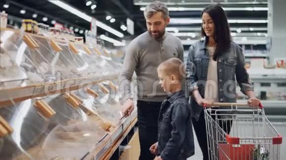 年轻的家庭在超市的面包店挑选面包小男孩从塑料容器里拿面包视频的预览图