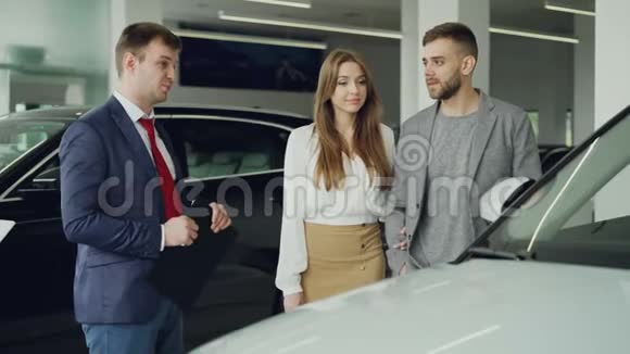 友好的汽车推销员正在和自信的年轻人谈论新车型而漂亮的女人则在谈论视频的预览图
