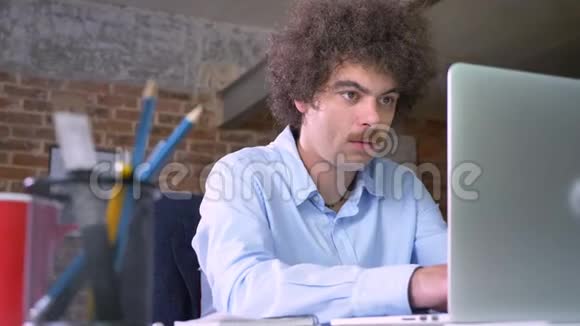 严肃的书呆子商人留着胡子和卷发手提电脑做笔记坐在现代办公室里视频的预览图