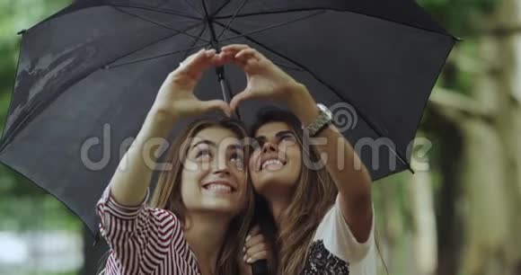 两个漂亮漂亮的女士在伞下特写用手做一颗心视频的预览图