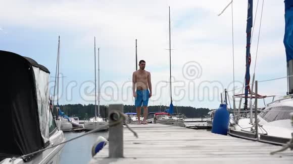 一个穿短裤的年轻人走在码头游艇和船的背景上视频的预览图