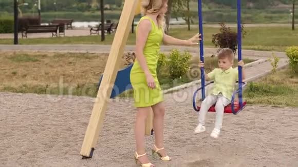 夏天年轻漂亮的女人把她的小儿子卷在公园的秋千上视频的预览图
