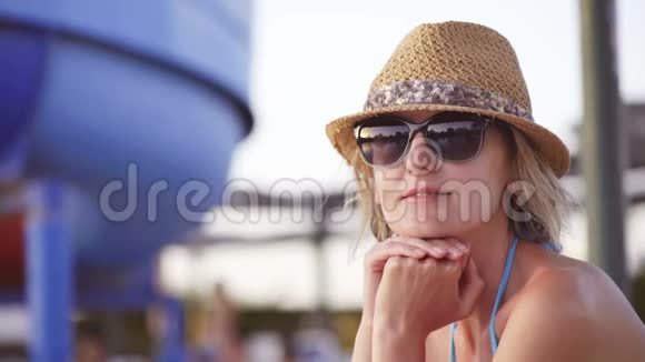 穿泳装的女人坐在游泳池旁看着镜头微笑视频的预览图