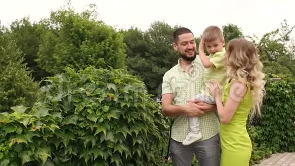 一个年轻的家庭在一个公园里的绿树丛中散步视频的预览图
