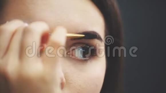 美丽的年轻女孩站在黑色的背景上在这期间照镜子用刷子使眉毛视频的预览图