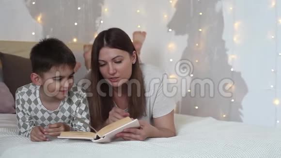 妈妈躺在床上睡觉前给孩子读一本书然后吻他视频的预览图