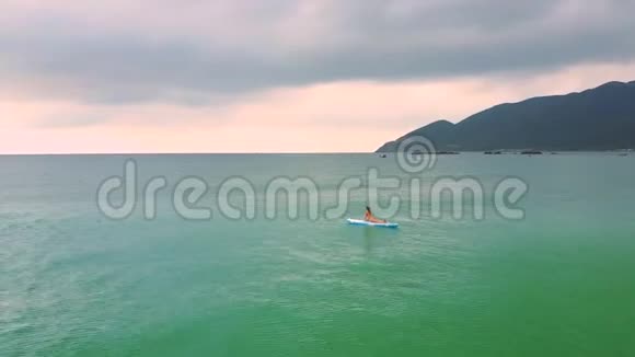 女孩的身影躺在漂浮在蔚蓝的海洋中的桨板上视频的预览图