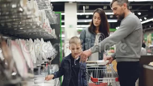 笑容满面的一家人在超市的厨具部门买碗和盘子他们从货架上拿盘子视频的预览图