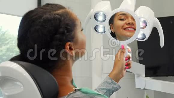 开朗的非洲女人微笑着在镜子里审视她健康的微笑视频的预览图