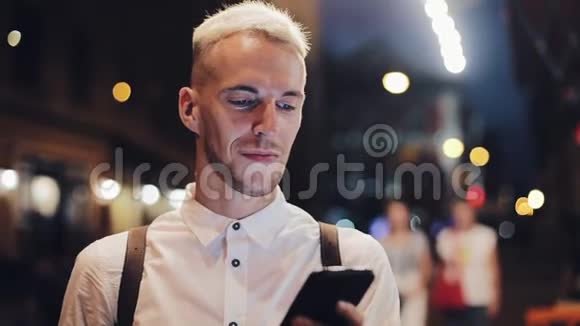 微笑的人在夜间城市使用智能手机英俊的年轻人晚上用智能手机流动通信视频的预览图