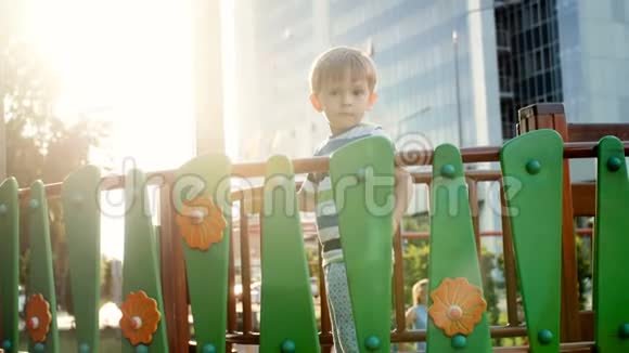 日落时分站在操场上的木桥上一个可爱微笑的幼儿男孩的4k镜头视频的预览图