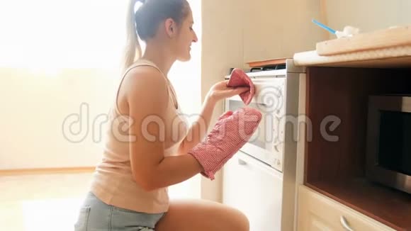 4k镜头年轻微笑的家庭主妇用硅胶烘焙形式在厨房的热烤箱里放馅饼视频的预览图