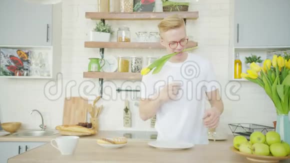 美丽的金发男人早上在厨房为他的女朋友做早餐视频的预览图