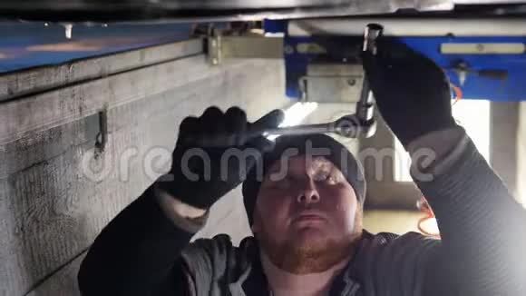汽车服务厚机修工站在汽车下面的检查坑里用工具工作视频的预览图