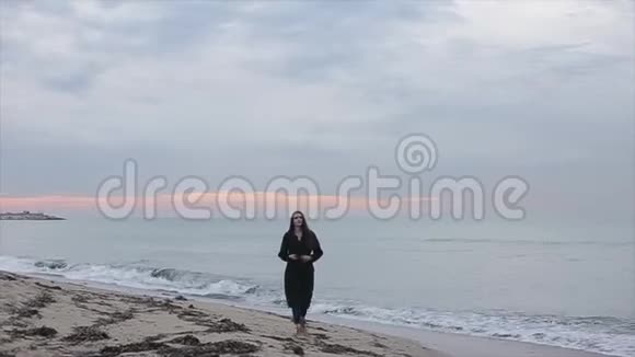 日出时一个穿着长春衣的漂亮女孩在海滩上散步视频的预览图