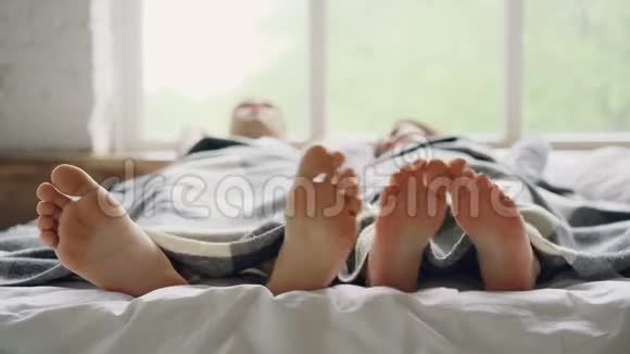 可爱的情侣躺在床上躺在毯子下聊天专注于赤脚触摸和抚摸对方视频的预览图