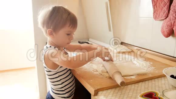 有趣的幼儿男孩用大木擀面杖在厨房台面上擀制馅饼面团的4k视频视频的预览图