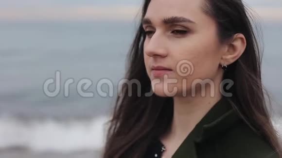 一个美丽的微笑女孩的特写穿着绿色外套看着海滩上的一边背景模糊重点视频的预览图