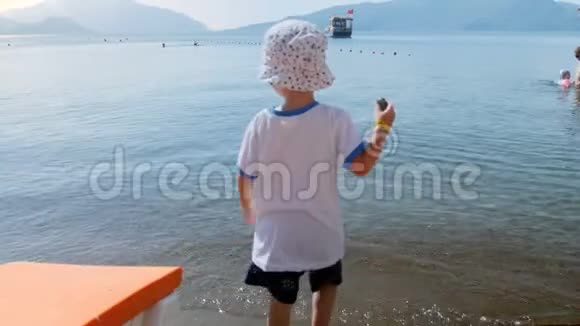 小男孩在沙滩上平静的海面上扔石头的4k镜头视频的预览图