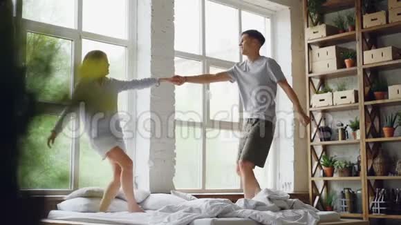 可爱的情侣在床上跳舞在现代的轻屋里拥抱在一起快乐的年轻人视频的预览图