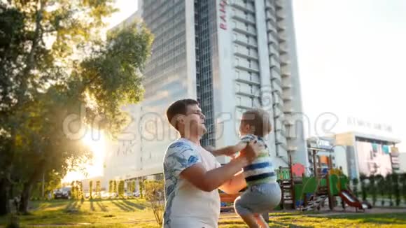 4k视频快乐的年轻父亲抱着他蹒跚学步的小儿子在公园日落时抛空视频的预览图