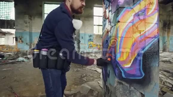 在旧建筑内破损的柱子上画涂鸦的有创意留胡子的家伙的倾斜镜头视频的预览图