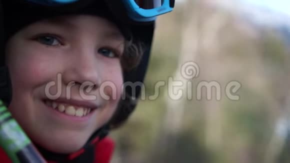 穿着头盔和护目镜的小学生坐在滑雪缆车舱里孩子开心地笑了在山上度过有趣的假期视频的预览图