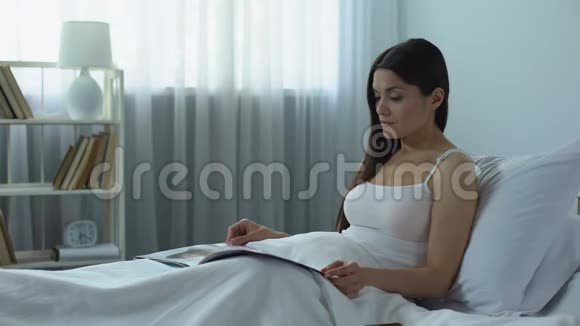 美丽的女人带着兴趣阅读光滑的杂志在家愉快的消遣视频的预览图
