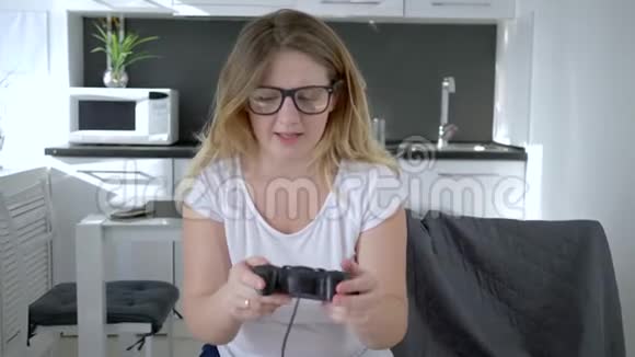 现代游戏戴眼镜的女孩坐在家里的椅子上玩电子游戏视频的预览图