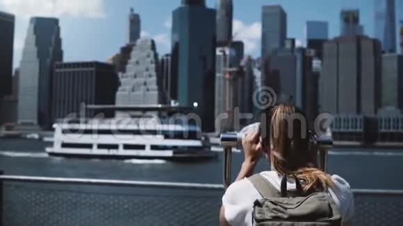 在纽约曼哈顿金融中心的史诗全景下年轻的旅行者女孩通过硬币望远镜观看视频的预览图