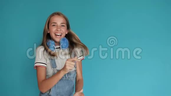 一个长着大白牙在蓝色背景上跳舞的小女孩带着明亮的蓝色耳机的少女视频的预览图