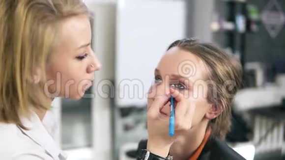 化妆工作化妆师和模特女孩化妆短发白皙化妆师画眼线下眼睑视频的预览图