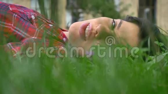 快乐的年轻女子留着黑色短发微笑着躺在草地上开朗友好视频的预览图