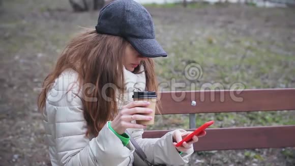 戴帽子的女孩用电话在长凳上喝咖啡视频的预览图