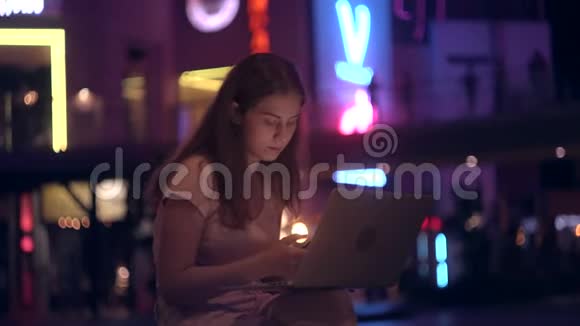 那女孩在夜市里用笔记本电脑在办公室外工作视频的预览图